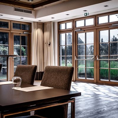 Ein eleganter Konferenzraum mit Holzmöbeln, großen Fenstern und natürlichem Licht. Reihenweise Stühle und Tische, jeweils mit Notizblock und Wasserglas.