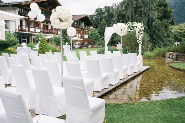 Elegante Outdoor-Hochzeitszeremonie mit weißen Stühlen und Blumen