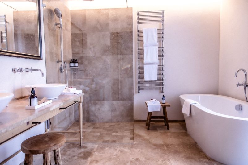Ein modernes Badezimmer mit einer freistehenden Badewanne, einem großen Spiegel, Doppelwaschbecken und Handtuchhalter. Neutrale Farben dominieren den Raum.
