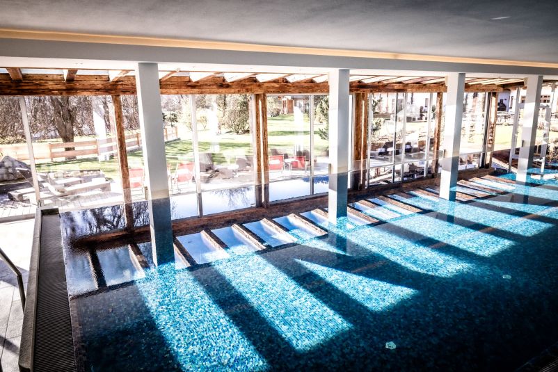 Beleuchtetes Hallenbad mit Blick auf den grünen Außenbereich