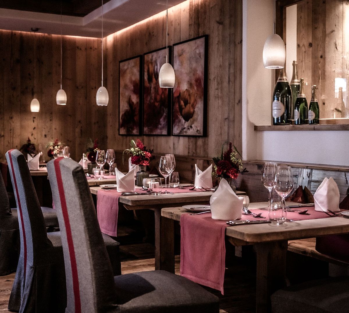 Gemütliches Restaurant mit Holzwänden, stilvoll gedeckten Tischen, weichen Polsterstühlen und sanfter Beleuchtung. Große Champagnerflaschen als Dekoration.