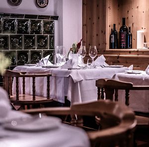 Gemütliches Restaurantambiente mit weiß gedeckten Tischen und elegant gefalteten Servietten. Im Hintergrund sind Weinflaschen in einem Holzkabinett zu sehen.