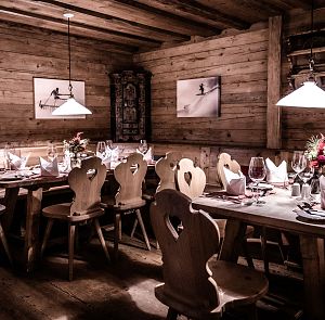 Gemütliches alpines Restaurant mit Holzwänden und rustikalen Möbeln. Zwei lange Holztische sind elegant gedeckt, mit Weingläsern und Blumenschmuck.