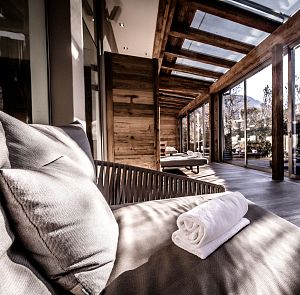 Ein luxuriöser, moderner Spa-Bereich mit großen Glasfenstern und Holzelementen. Eine weiße Handtuchrolle liegt auf einer bequemen Liege, umgeben von natürlichem Licht.