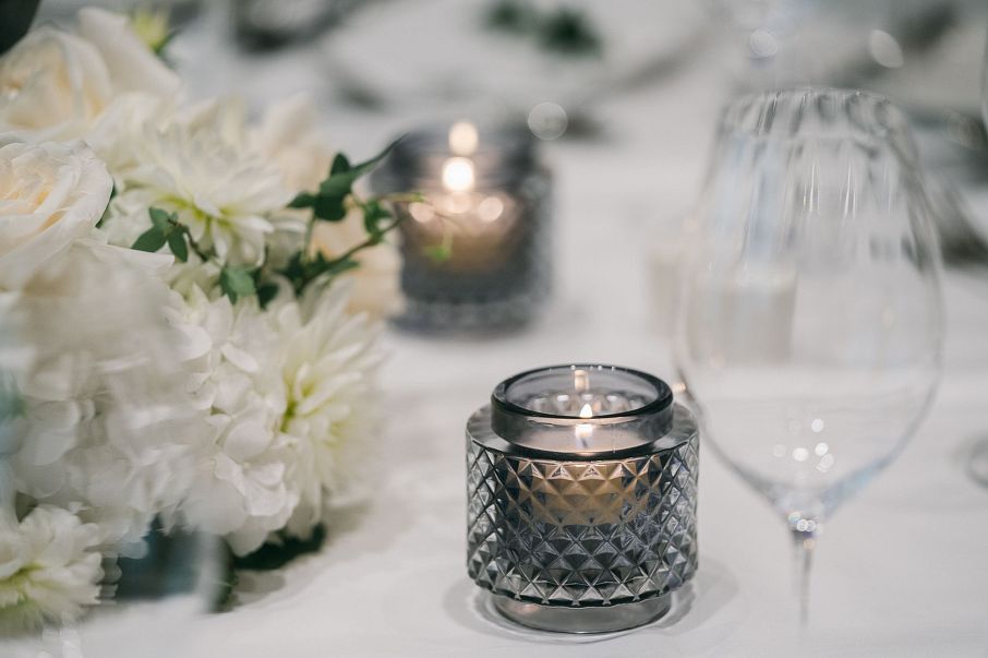 Edler Tischgedeck mit silbernem Windlicht, weißen Blumen und eleganten Gläsern. Die sanfte Beleuchtung schafft eine gemütliche, feierliche Atmosphäre.