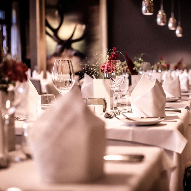 Elegantes Restaurant mit weiß gedeckten Tischen, stilvoller Dekoration und sanfter Beleuchtung. Weingläser, kerzenartige Leuchten und Blumenarrangements schaffen eine gehobene Atmosphäre.