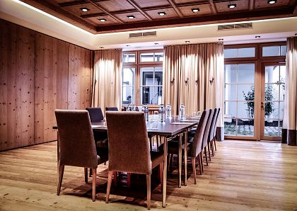 Eleganter, moderner Konferenzraum mit Holzwänden und -boden. Ein rechteckiger Tisch mit acht Stühlen steht im Zentrum. Große Fenster mit Vorhängen im Hintergrund.