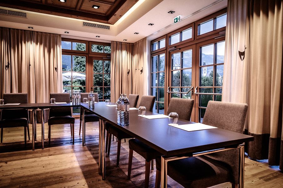 Eleganter Konferenzraum mit Holzboden, großen Fenstern, die viel Tageslicht hereinlassen, und dunklen Holztischen, die mit Wasserkarafeln und Schreibutensilien gedeckt sind.