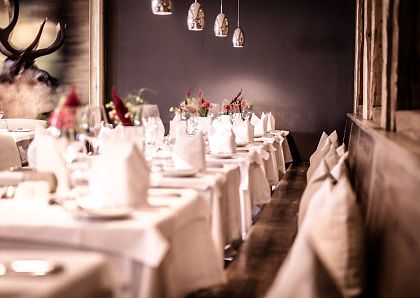 Elegantes Restaurant mit langen Reihen weiß gedeckter Tische. Dezente Beleuchtung, Blumenarrangements und Hirschbilder schaffen eine gemütliche Atmosphäre.