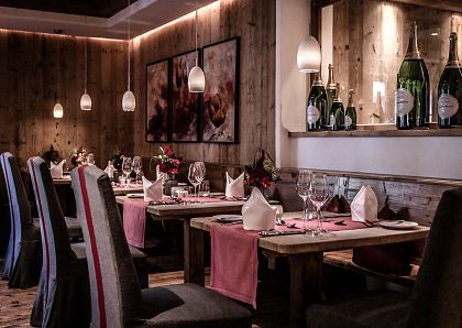 Gemütliches Restaurant mit Holzwänden, stilvoll gedeckten Tischen, weichen Polsterstühlen und sanfter Beleuchtung. Große Champagnerflaschen als Dekoration.