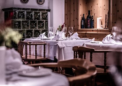 Gemütliches Restaurantambiente mit weiß gedeckten Tischen und elegant gefalteten Servietten. Im Hintergrund sind Weinflaschen in einem Holzkabinett zu sehen.