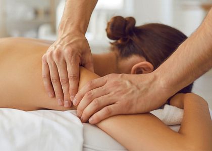 Eine Person erhält eine professionelle Rückenmassage in einem ruhigen Raum. Die Hände des Masseurs kneten sanft die Schulterpartie, während die Person entspannt liegt.