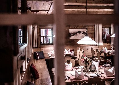 Gemütliches Restaurant mit Holzmöbeln, weiß gedeckte Tische mit Servietten, Lichter sorgen für eine warme Atmosphäre. Rustikaler Charme durch Holzwände.