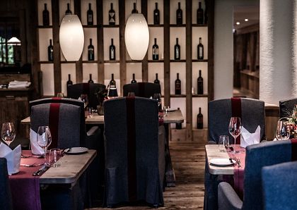 Elegantes Restaurant mit Holzelementen, stilvoll gedeckten Tischen und stimmungsvoller Beleuchtung. Im Hintergrund eine Wand mit dekorativen Weinflaschen.