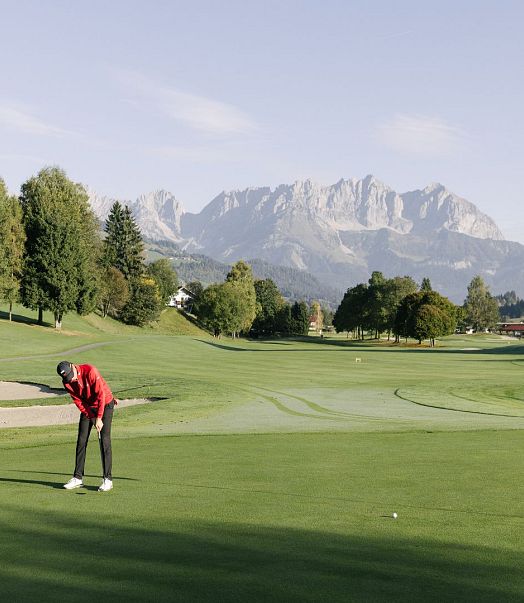 Mann am Golfplatz bei Morgenstimmung im Sommer mit Wildem Kaiser im Hintergrund