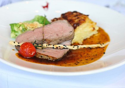 Ein Gourmet-Teller mit saftigem Rinderfilet, knusprigem Gratin und frischem Salat auf einem weißen Teller, im Hintergrund verschwommene Weingläser.