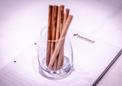 Ein Glas mit mehreren braunen, holzartigen Stiften steht auf einem Notizblock mit der Aufschrift "Hotel Kitzhof". Der Hintergrund ist unscharf.