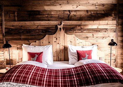 Gemütliches Schlafzimmer mit rustikaler Holzvertäfelung, einem großen Bett mit rot-weiß karierten Decken und dekorativen roten Kissen mit Hirschmotiv.