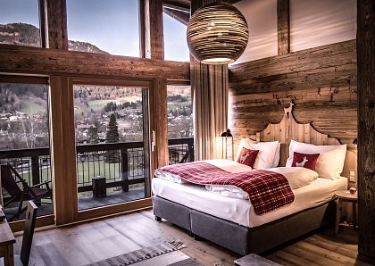Gemütliches Schlafzimmer mit Doppelbett in rustikalem Stil. Holzwände, große Fenster mit Blick auf die Landschaft und eine elegante Hängelampe.