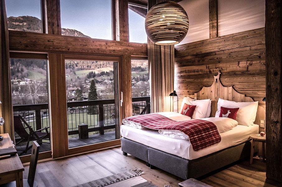 Gemütliches Schlafzimmer mit Doppelbett in rustikalem Stil. Holzwände, große Fenster mit Blick auf die Landschaft und eine elegante Hängelampe.