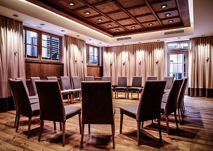 Ein eleganter Konferenzraum mit Holzboden und einer kreisförmigen Anordnung von Stühlen. Der Raum ist durch Vorhänge und eine Holzdecke gemütlich gestaltet.