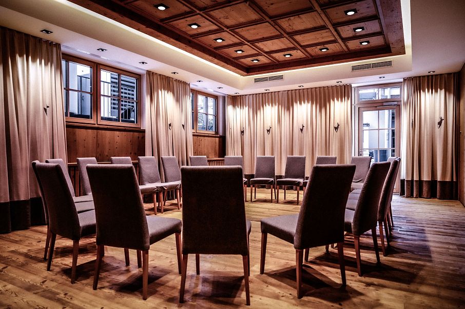 Ein eleganter Konferenzraum mit Holzboden und einer kreisförmigen Anordnung von Stühlen. Der Raum ist durch Vorhänge und eine Holzdecke gemütlich gestaltet.