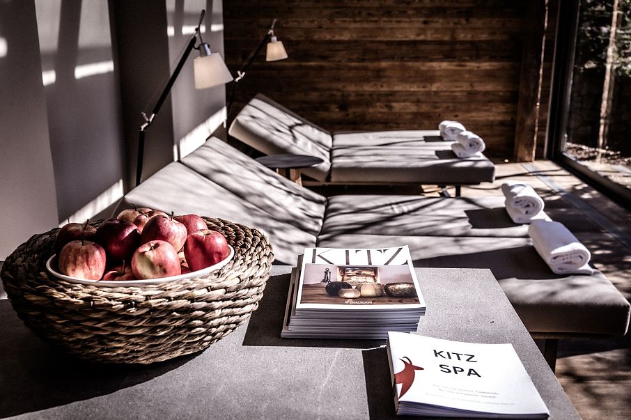 Ein luxuriöser Spa-Bereich mit zwei Liegestühlen, sorgfältig gerollten Handtüchern und einem Tisch mit einem Korb voller roter Äpfel und einem Katalog.