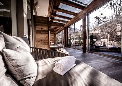 Ein luxuriöser, moderner Spa-Bereich mit großen Glasfenstern und Holzelementen. Eine weiße Handtuchrolle liegt auf einer bequemen Liege, umgeben von natürlichem Licht.